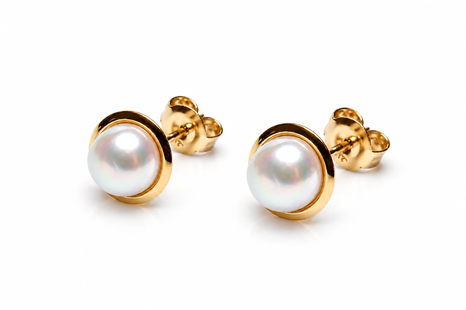 Close-up of two small freshwater pearl stud earrings set in plain polished 9ct gold, shown on a bright white background.