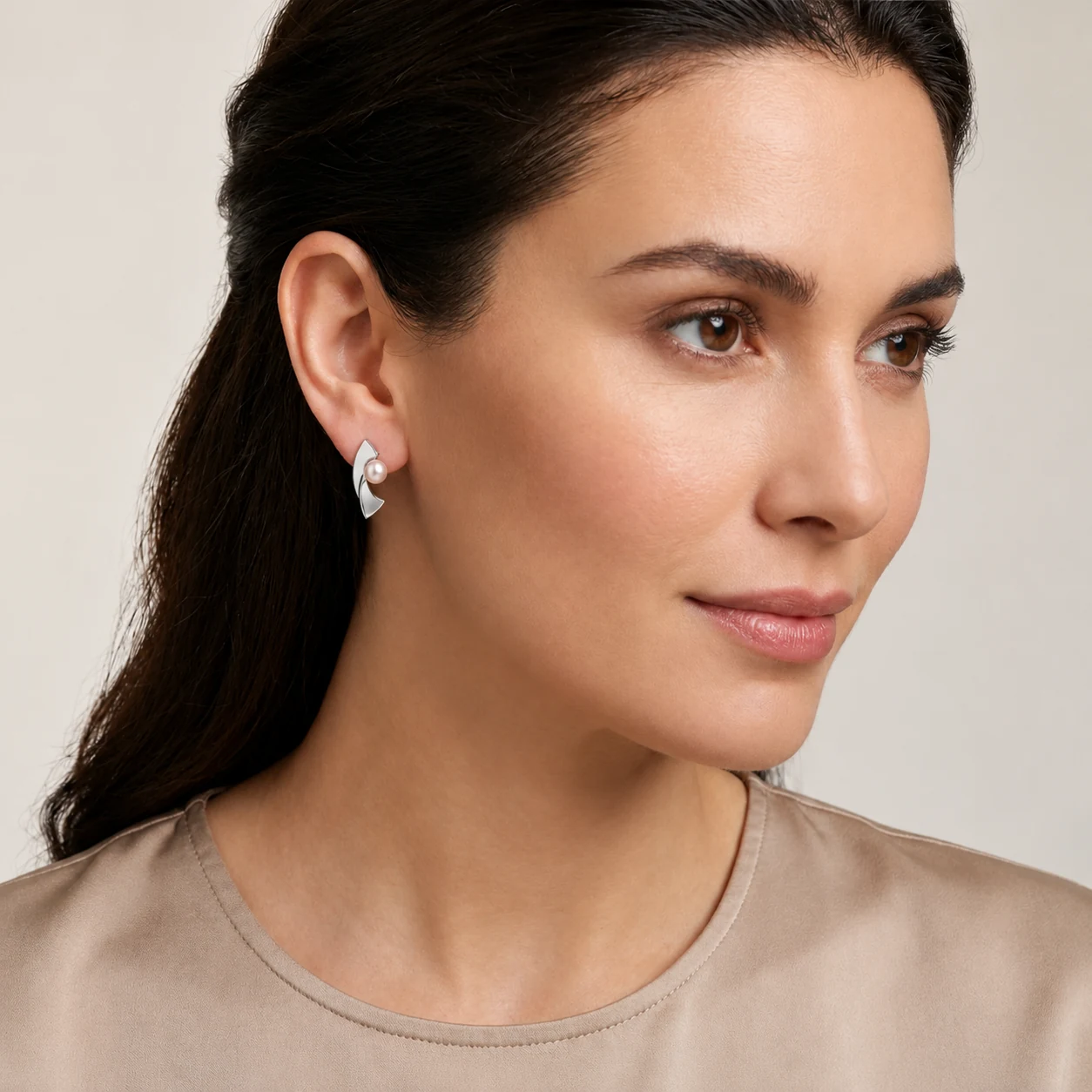 A woman models a silver contemporary curved stud earring with a pink freshwater cultured pearl, shown in close-up.